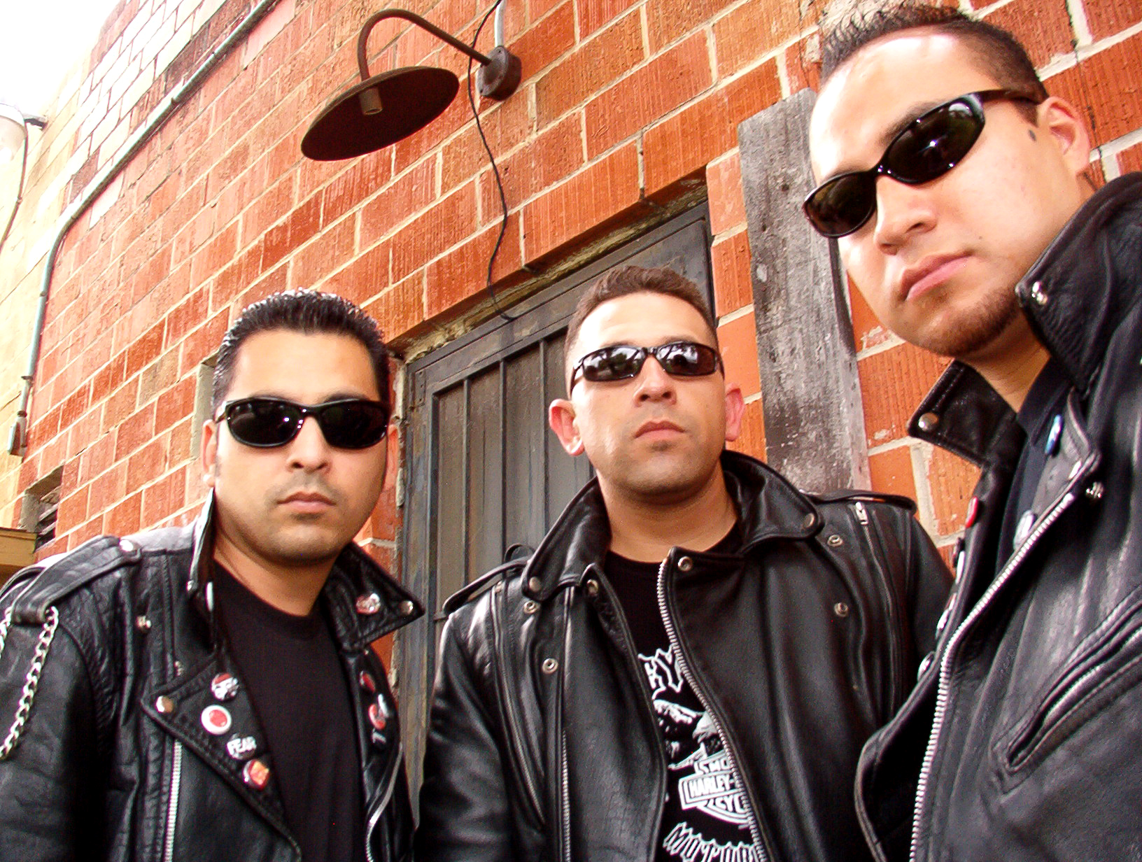 Dementers promo photo: three members in leather jackets and sunglasses against a red brick wall
